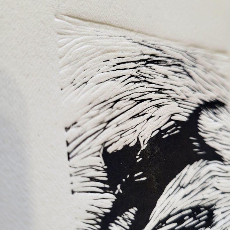 K&ouml;nnte beinhalten: Nahaufnahme einer strukturierten, cremefarbenen Oberfl&auml;che mit einem schwarz-wei&szlig;en Grafikdesign. Das Design zeigt ein stilisiertes, abstraktes Bild mit einer Kombination aus schwarzen Vollformen und wei&szlig;en, linearen Details. Das Kunstwerk hat eine handgemachte, k&uuml;nstlerische Ausstrahlung.