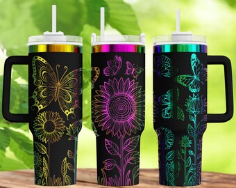 Op de afbeelding: Drie zwarte geïsoleerde bekers met handvatten, elk met een kleurrijk bloemen- en vlinderontwerp. De ontwerpen omvatten een zonnebloem, vlinders en andere bloemen. Elke beker heeft een wit rietje en een deksel met een metallic regenboogrand.