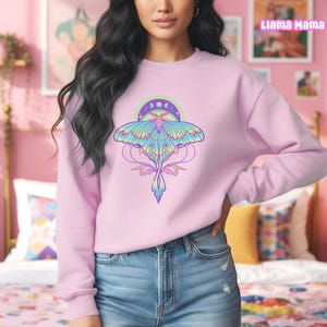May include: A light pink sweatshirt featuring a colorful moth design with a crescent moon and star accents. The moth has blue, green, and purple wings. The text "Llama Mama" is visible in the upper right corner.