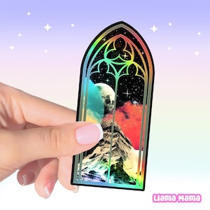 May include: A holographic sticker shaped like a gothic arched window featuring a night sky with a moon, stars, and a mountain range. The design includes vibrant red, blue, and yellow clouds set against a dark background with a metallic finish.