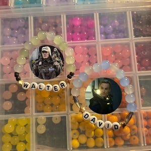 May include: Two beaded bracelets with the names "WALTER" and "DAVID" spelled out in white letter beads. Each bracelet features a circular image of a person. The beads are various colors, including green, blue, and white.