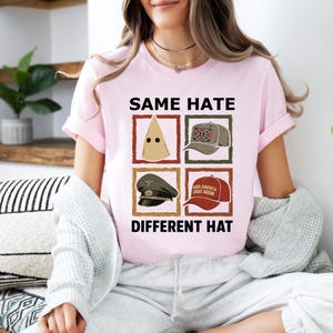 May include: Light pink t-shirt with the text "SAME HATE DIFFERENT HAT" and images of a hood, a hat with a Confederate flag, a military cap, and a red "Make America Great Again" hat.