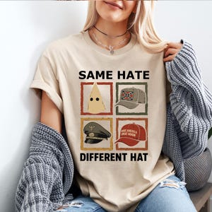May include: Beige t-shirt with the text "SAME HATE DIFFERENT HAT" and four framed images of hats. The images include a pointed hood, a Confederate flag cap, a military cap, and a "MAKE AMERICA GREAT AGAIN" cap.