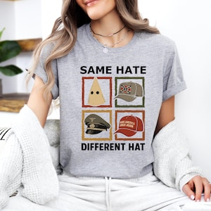May include: A gray t-shirt with the text "SAME HATE DIFFERENT HAT" and four images of different hats. The hats include a KKK hood, a Confederate flag hat, a military hat, and a "Make America Great Again" hat.
