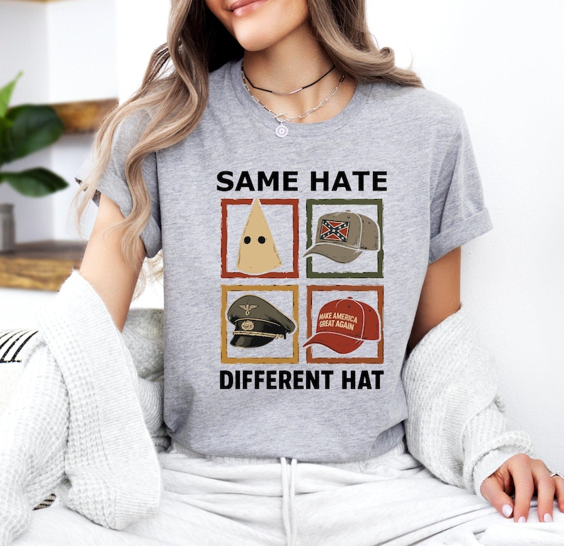 May include: A gray t-shirt with the text "SAME HATE DIFFERENT HAT" and four images of different hats. The hats include a KKK hood, a Confederate flag hat, a military hat, and a "Make America Great Again" hat.