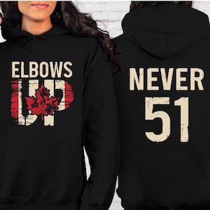 May include: Black hooded sweatshirt with the text "Elbows Up" and a red maple leaf on the front. The back of the sweatshirt has the text "Never 51" in white.