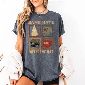 May include: Dark gray t-shirt with the text "SAME HATE DIFFERENT HAT" and images of a KKK hood, a Confederate flag hat, a military cap, and a "Make America Great Again" hat.