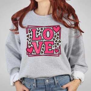 May include: A gray sweatshirt with the word "LOVE" in pink letters. The letter "O" has a zebra print, and the letters "L" and "VE" have a polka dot pattern. Pink hearts are on the sweatshirt.