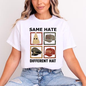 May include: White t-shirt with the text "SAME HATE DIFFERENT HAT" above and below four images of hats. The hats include a pointed hood, a baseball cap with a Confederate flag, a military cap, and a red baseball cap with the text "MAKE AMERICA GREAT AGAIN."