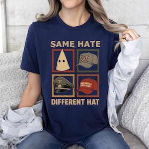 May include: Navy blue t-shirt with the text "SAME HATE DIFFERENT HAT" and four images of hats. The hats include a white hood, a baseball cap with a Confederate flag, a military hat, and a red "Make America Great Again" hat.
