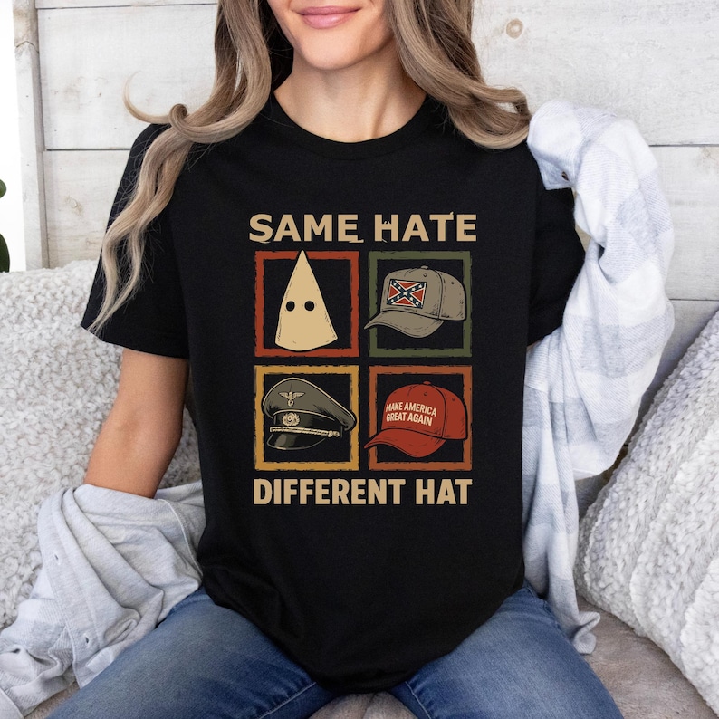 May include: Black t-shirt with the text "SAME HATE DIFFERENT HAT" and images of a KKK hood, a Confederate flag hat, a military cap, and a "Make America Great Again" hat. The shirt is worn by a person.