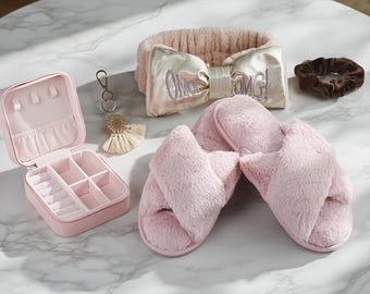 May include: A collection of self-care items, including a pink jewelry box, a fluffy pink headband with "OMG!" text, a brown scrunchie, a keychain with a tassel, and pink cross-strap slippers. The items are arranged on a marble surface.