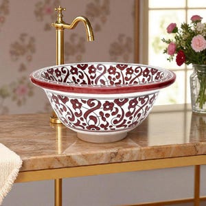 May include: A decorative ceramic sink with a white base and a wide, burgundy rim. The sink features a repeating floral pattern in burgundy against a white background. A gold faucet is positioned to the left of the sink.