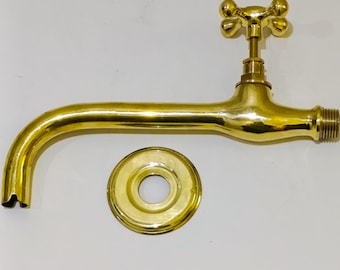Puede incluir: Un grifo de latón brillante con un caño curvo y un mango de cuatro pétalos. Una brida circular a juego se encuentra debajo. El grifo tiene un extremo roscado para la conexión. El diseño es vintage.