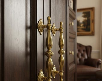 Puede incluir: Primer plano de un armario de madera marrón oscuro con tiradores dorados ornamentados. Los tiradores tienen un diseño vintage detallado. El armario parece ser parte de un mueble más grande, posiblemente una estantería o un armario.