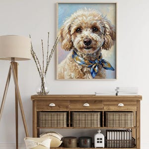 May include: A framed oil painting of a fluffy, light brown dog with a blue and yellow patterned scarf. The dog has a friendly expression and is set against a soft, pastel background. The artwork is displayed above a wooden console table.
