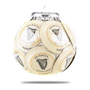 May include: A Christmas ornament shaped like a soccer ball made from Guinness beer bottle caps. The ornament is white with black and gold accents. The caps feature the Guinness logo, which includes a harp and the words "Guinness Extra Stout".