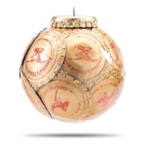 May include: A gold Christmas ornament made from bottle caps. The caps are from a brewery and feature the text "America's Oldest Brewery" and a red bird logo.