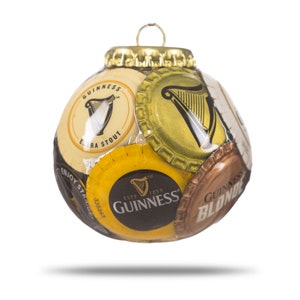 May include: A Christmas ornament made from multiple Guinness beer bottle caps. The ornament is round and features the Guinness logo and harp design. The ornament is gold, black, and white.