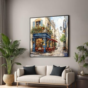 Puede incluir: Una pintura de acuarela de una cafetería parisina con toldos azules y blancos, sillas y mesas rojas y una calle adoquinada. La cafetería se llama "Le Petit Gourmand" y tiene un letrero con un toldo a rayas rojas y blancas.