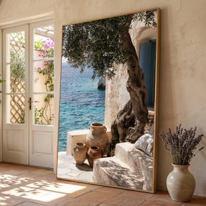 May include: A large rectangular floor mirror with a thin gold frame displaying a high-resolution print of a Mediterranean coastal scene featuring an olive tree, stone steps, terracotta pots, and a view of the blue sea under bright sunlight.