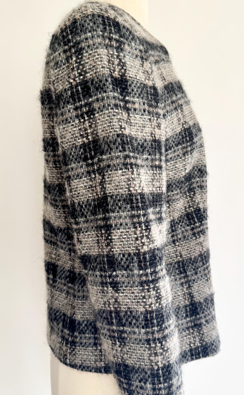 May include: A black, grey, and white plaid jacket. The jacket has a classic design with a round neckline and long sleeves. The fabric appears to be a woven tweed or similar material, offering a warm and stylish look. The jacket is a stylish garment.