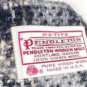 May include: Close-up of a woven fabric with a label. The label reads "PETITE PENDLETON" with additional text indicating it's made of 100% virgin wool in the USA. The fabric has a mix of black, white, and beige threads.