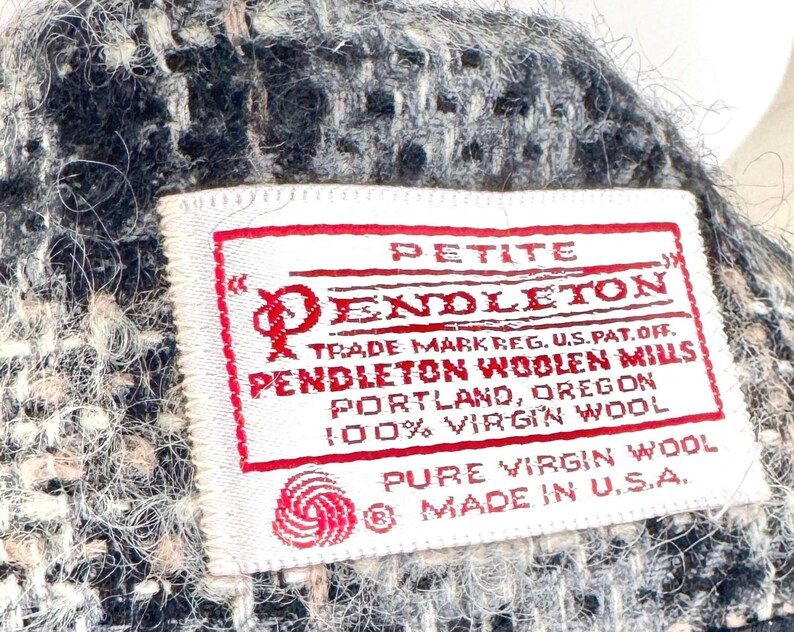 May include: Close-up of a woven fabric with a label. The label reads "PETITE PENDLETON" with additional text indicating it's made of 100% virgin wool in the USA. The fabric has a mix of black, white, and beige threads.