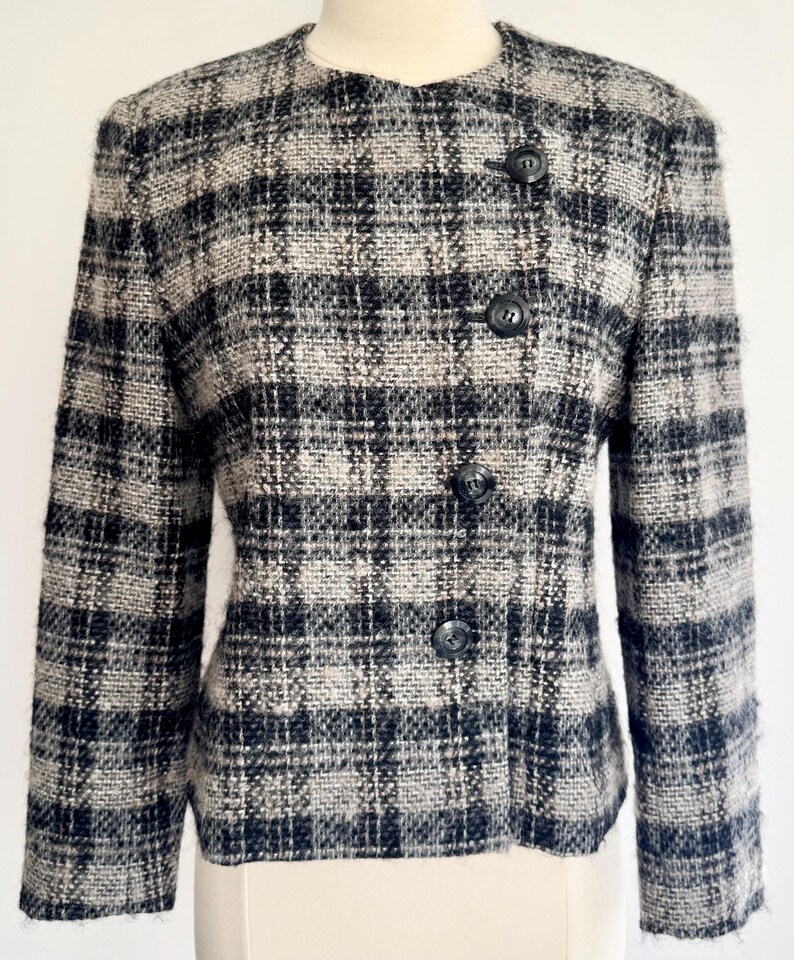 May include: A black, grey, and white checked jacket with a round collar and three black buttons. The jacket is made of a textured fabric and has long sleeves. The jacket is displayed on a mannequin.