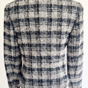 May include: A black, white, and grey plaid blazer. The jacket has a classic design with a tailored fit. The fabric appears to be a woven tweed. The blazer is displayed on a mannequin.