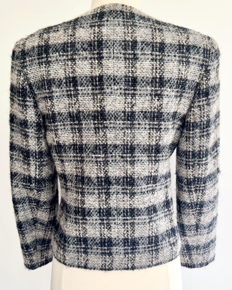 May include: A black, white, and grey plaid blazer. The jacket has a classic design with a tailored fit. The fabric appears to be a woven tweed. The blazer is displayed on a mannequin.