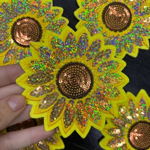 May include: Several yellow sunflower patches with brown centres and iridescent sequin petals are shown. The patches are embroidered with a detailed design, showcasing a vibrant and decorative floral theme.