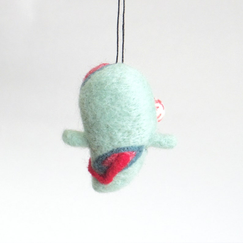 May include: A teal blue felt ornament with red and white accents. The ornament is shaped like a bird with a small beak and a tail.