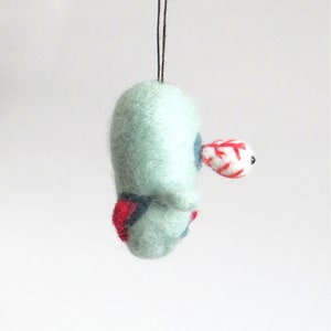 May include: A light blue felt ornament with a red and white striped eye and a black bead. The ornament is hanging from a black string.