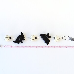 May include: A black and white Halloween garland with bats and white pom poms. The garland is 10 inches long and has a tag that says "fuzzbunn".