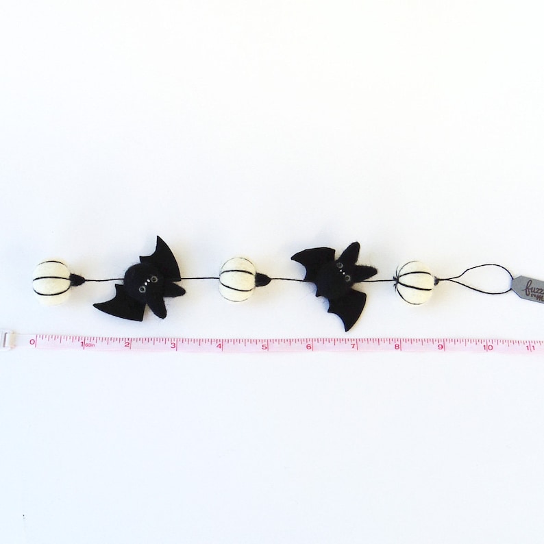 May include: A black and white Halloween garland with bats and white pom poms. The garland is 10 inches long and has a tag that says "fuzzbunn".