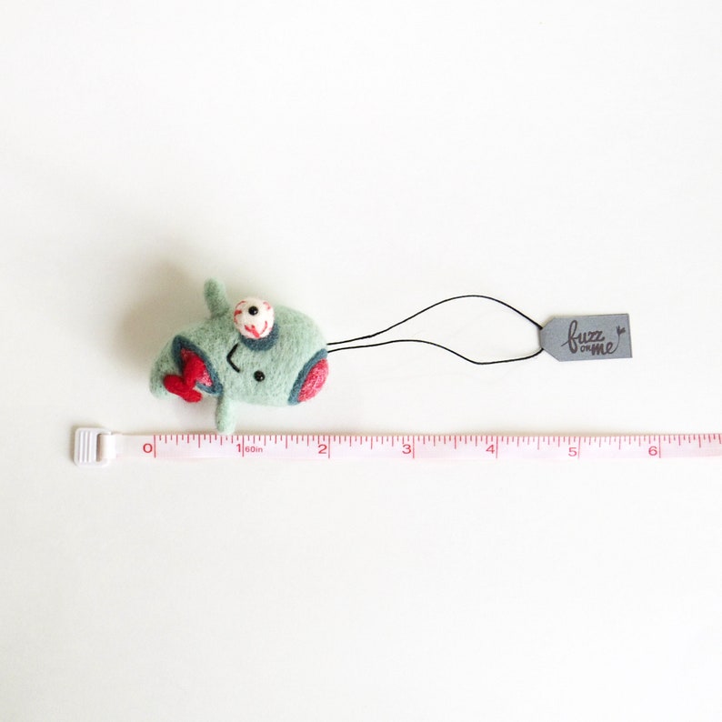 May include: Green felt zombie creature with a red heart, one eye, and a black mouth. The creature is attached to a black string with a gray tag that says "fuzz on me".