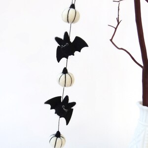Miniature short garland is hanging from a small tree branch. 3 white felt pumpkins with 2 black felted bats.