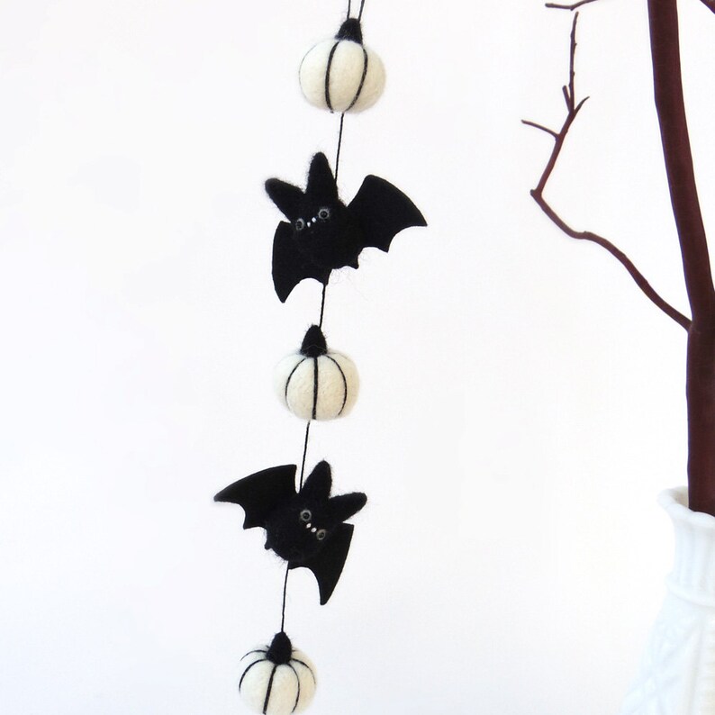 Miniature short garland is hanging from a small tree branch. 3 white felt pumpkins with 2 black felted bats.