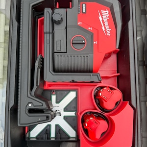 Puede incluir: Un kit de nivel láser Milwaukee negro y rojo en un estuche de transporte negro. El kit incluye un nivel láser rojo, dos baterías rojas y un soporte de montaje negro. El logotipo de Milwaukee es visible.