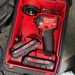 Peut inclure: Un kit de visseuse à chocs Milwaukee FUEL rouge et noir dans une mallette rigide noire. Le kit comprend la visseuse à chocs, deux batteries REDLITHIUM M18 de 3,0 Ah et d'autres accessoires. La mallette est ouverte, révélant les outils et les composants.
