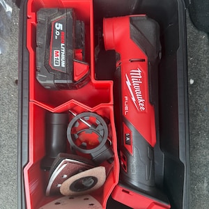 May include: A black and red Milwaukee FUEL multi-tool kit. The kit includes a red and black multi-tool, a 5.0 M18 REDLITHIUM battery, and various sanding attachments. The kit is stored in a black case with red compartments.