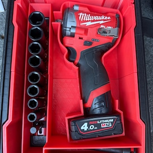 May include: A red and black Milwaukee M12 FUEL impact wrench and socket set in a red storage case. The set includes various sockets and a 4.0 Ah battery. The case is open, revealing the tools neatly organized.