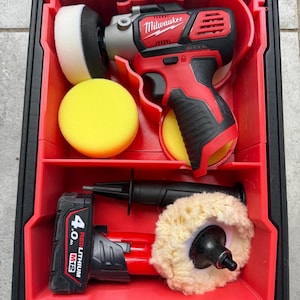 Pode incluir: Um kit de detalhe Milwaukee M12 vermelho e preto numa caixa preta e vermelha. O kit inclui uma polidora, almofadas de polimento e uma bateria. A caixa é dividida em compartimentos para guardar as ferramentas e acessórios.
