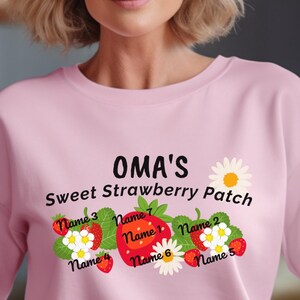 May include: Pink sweatshirt with the text "OMA'S Sweet Strawberry Patch" and a design of strawberries and flowers with names written on them.