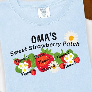 May include: Light blue t-shirt with the text "OMA'S Sweet Strawberry Patch" and a design of strawberries and flowers with names written on each strawberry.
