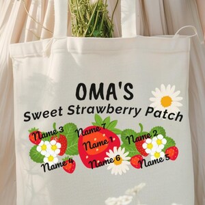 May include: A white canvas tote bag with the text "OMA'S Sweet Strawberry Patch" and a design of strawberries and daisies. The strawberries have names written on them.