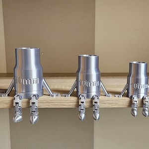 Könnte beinhalten: Ein Set aus sieben silberfarbenen, 3D-gedruckten, roboterartigen Figuren mit beweglichen Armen und Beinen. Jede Figur hat einen zylindrischen Körper mit dem Wort "Omme" darauf.