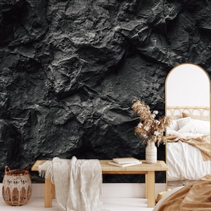 May include: A bedroom interior with a black and white rock wall mural, a wooden bench with a white throw blanket, a wicker basket, a vase with dried flowers, and a large arched mirror.