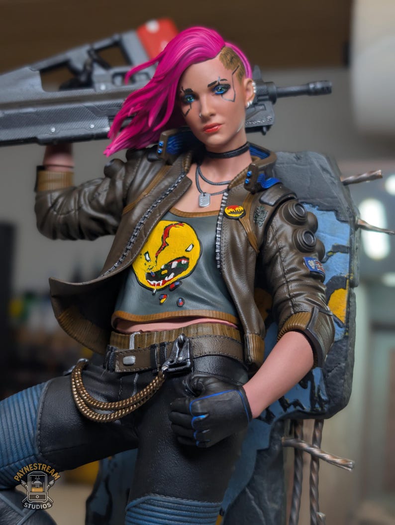May include: A collectible action figure featuring a character with bright pink hair, wearing a brown leather jacket over a gray crop top with a yellow graphic, black pants with a gold chain, and black gloves, holding a large black rifle.